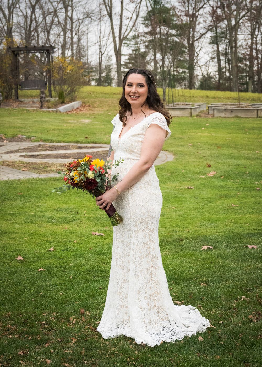 A lace wedding dress and autumn bouquet photographed outdoors in a garden setting.