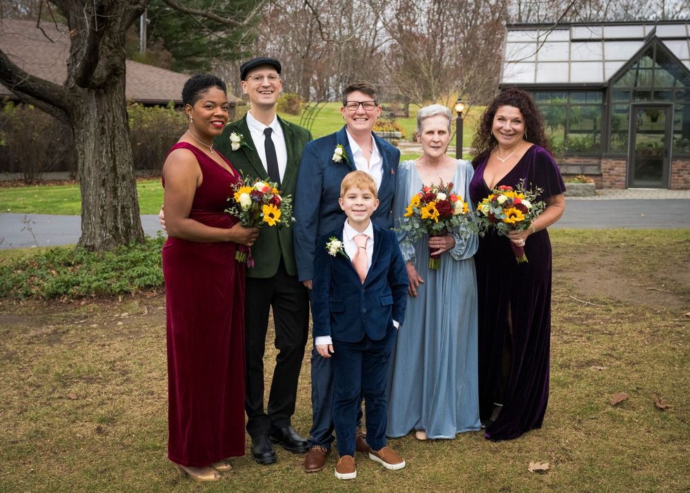 Wedding party poses outdoors with sunflowers and formal attire in an autumn setting.