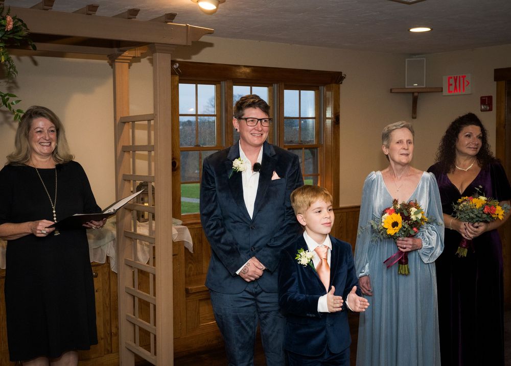 Wedding celebration group photo in an indoor venue with warm lighting.