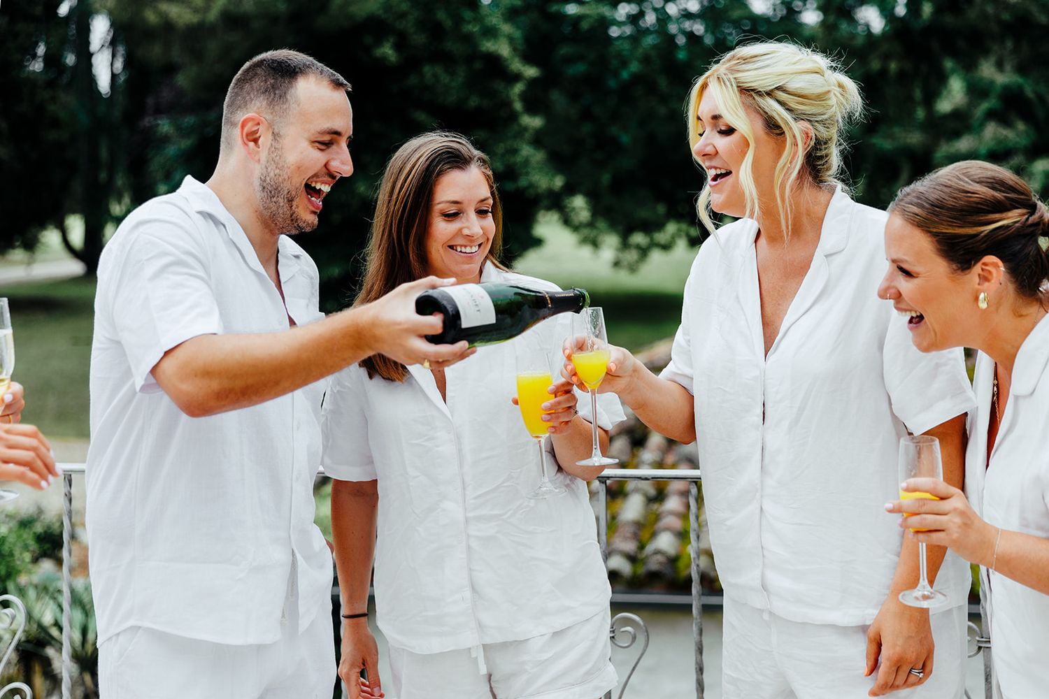 Group of people in white outfits toasting and celebrating with drinks at an outdoor gathering.