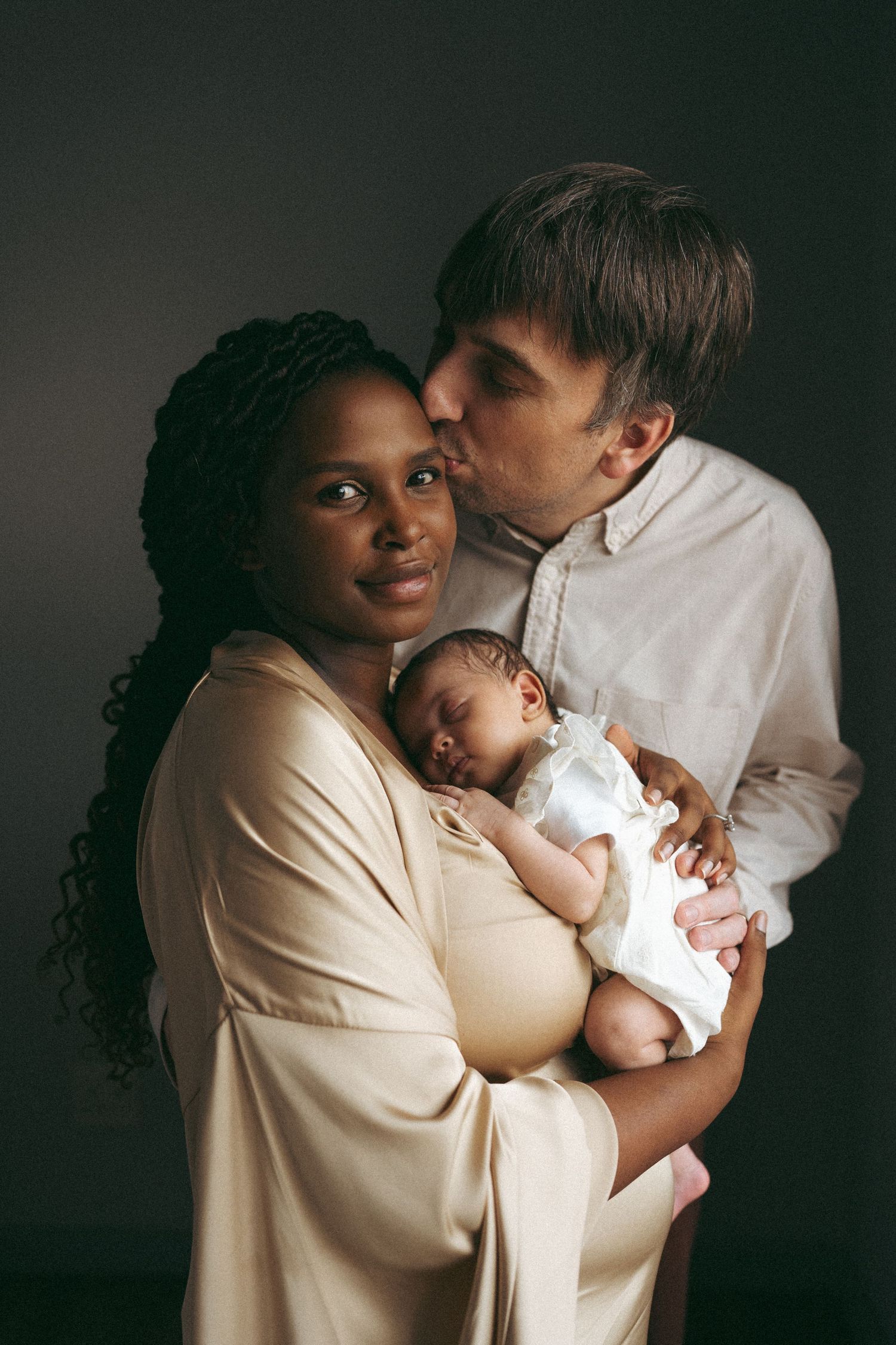 Tender family moment captured in soft lighting as parents cradle their newborn.