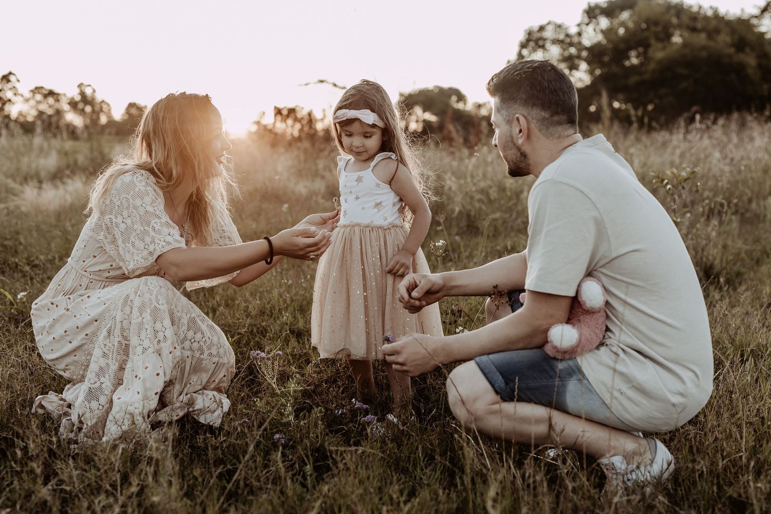 Family sitting together in a grassy field during golden hour sunset.