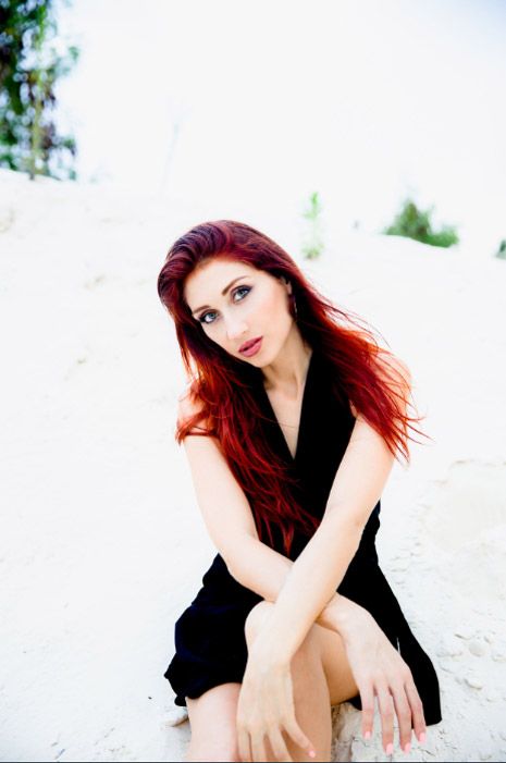A model with vibrant red hair poses in a black dress against a bright white background. Photo session.