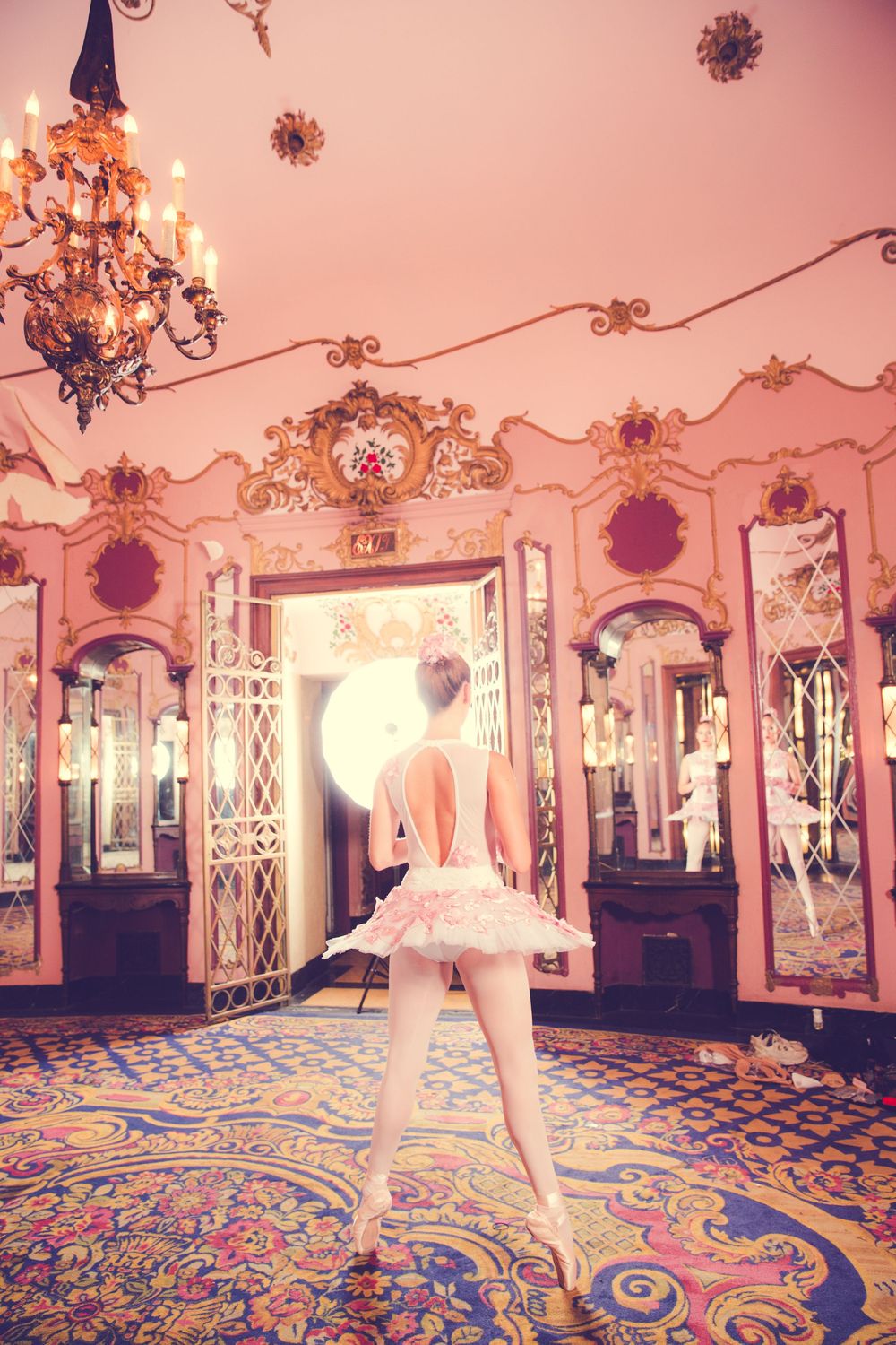 Dancer in white tutu performing on patterned carpet in ornate rococo-style room.