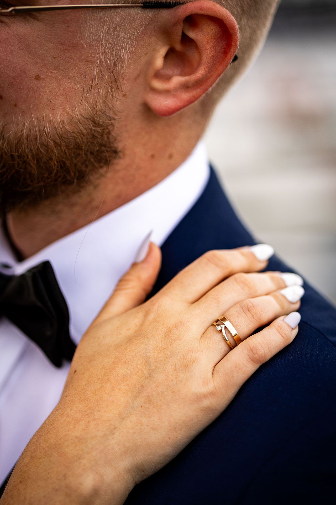 Close-up of a hand wearing a wedding ring resting on a navy suit with bow tie.