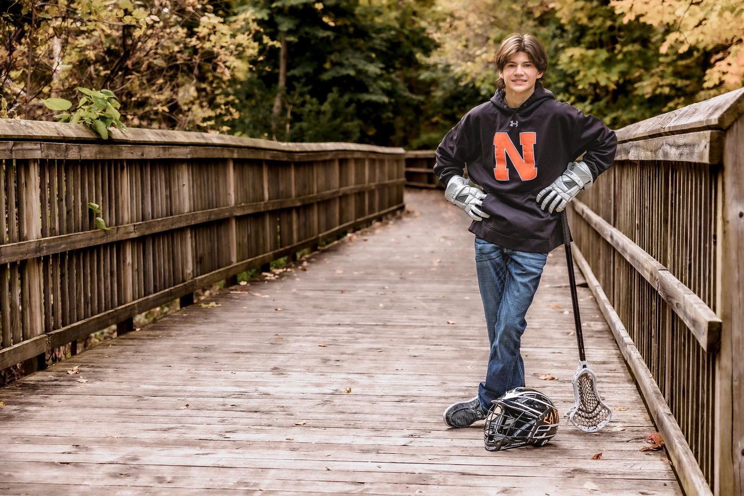 A person in jeans walks along a wooden boardwalk path through autumn foliage on a misty day.