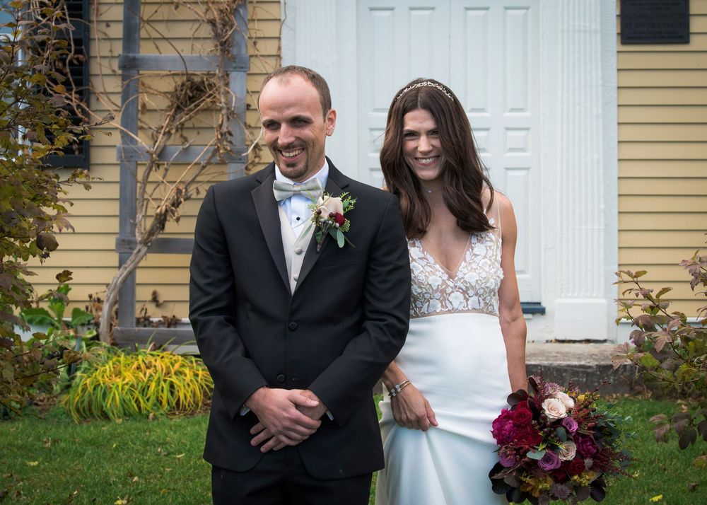 Wedding party poses for formal portraits in front of a yellow house with white doors.
