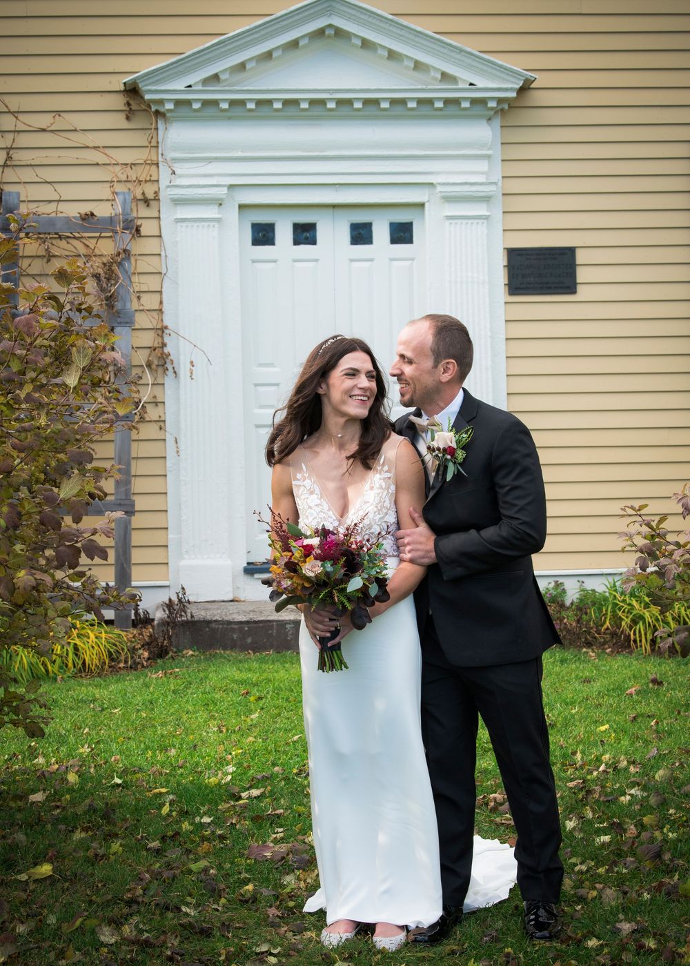 Couple sharing a moment in front of a yellow colonial house with white trim and columns.