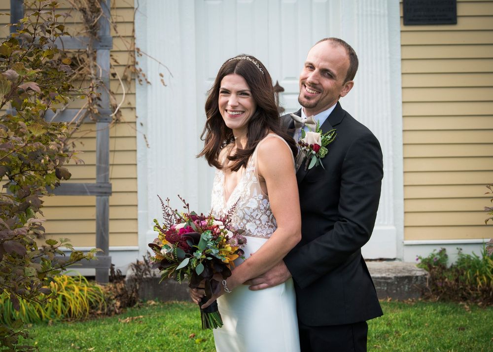 A romantic wedding moment captured in front of a classic yellow New England home.