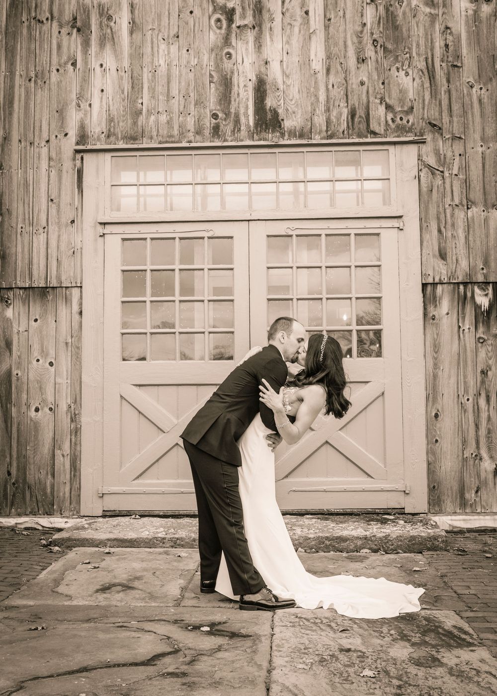 A romantic black and white wedding photo of a couple embracing in front of a rustic barn door.