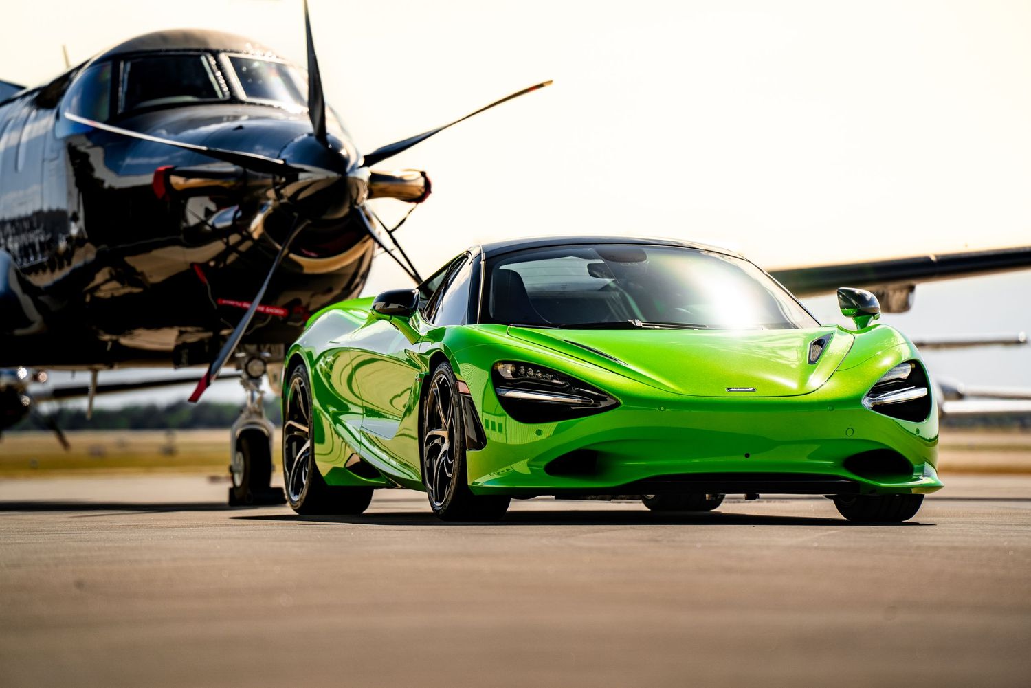 A sleek black McLaren supercar with a prominent rear wing silhouetted against a dramatic sunset sky.