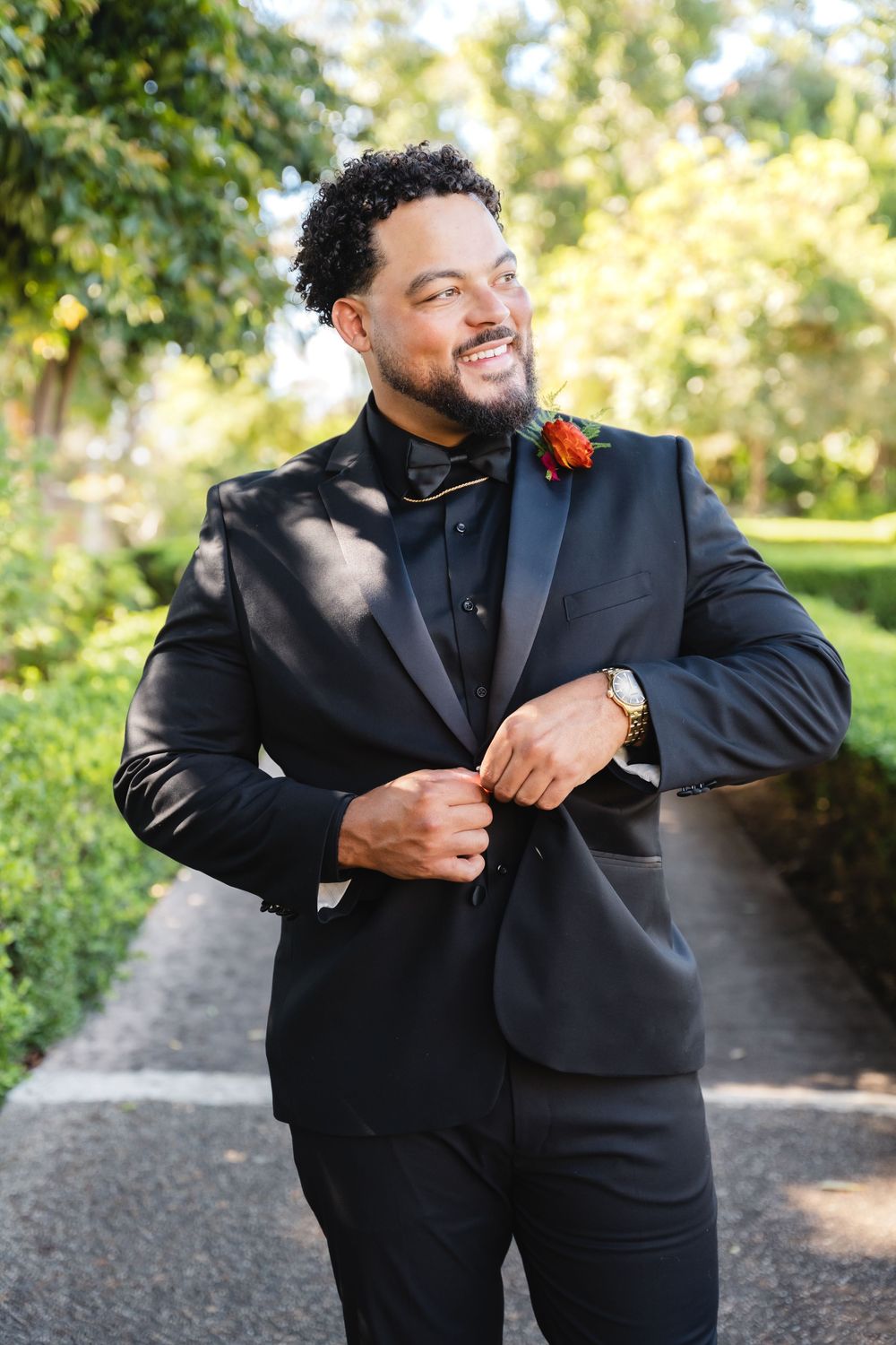Smiling groom puts on his jacket for wedding portraits at Alcázar Garden in Balboa Park