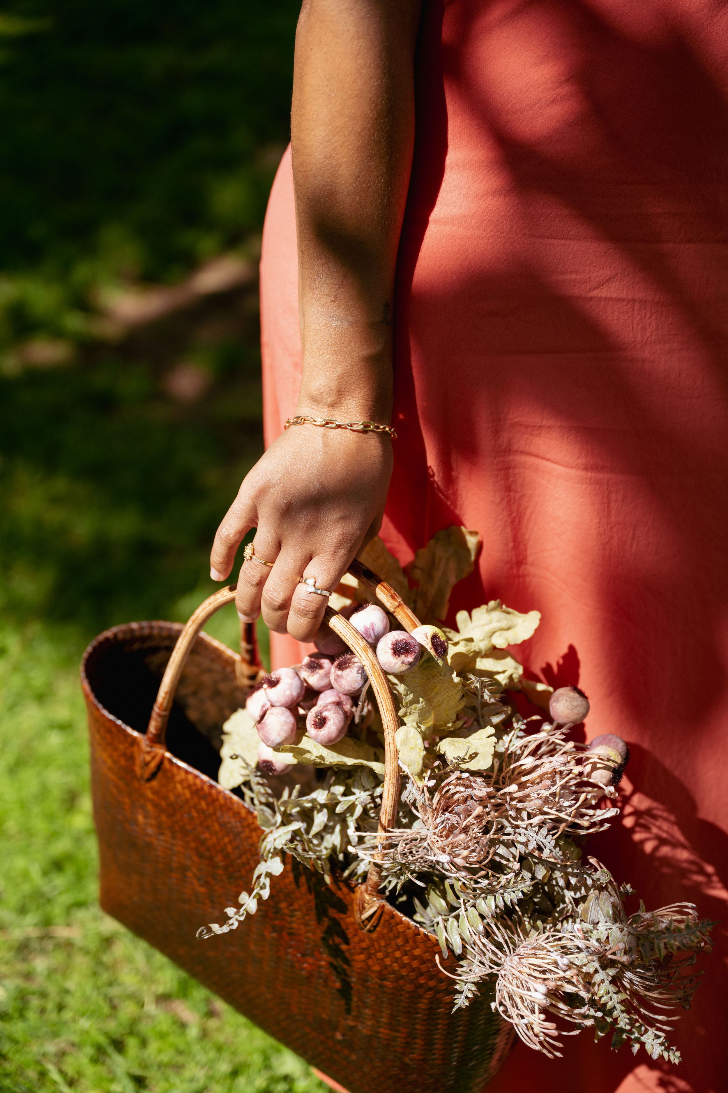 A rustic woven basket filled with delicate dried flowers and purple berries being carried in sunlit garden.