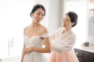 Two people share a joyful moment while preparing in an elegant white dressing room.