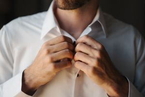 Close-up view of hands adjusting a white dress shirt collar in natural lighting.