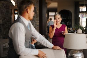 Two people sit at a bar counter engaged in conversation while one person holds a beverage.