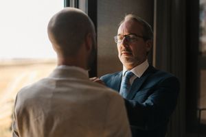 Two business professionals in suits having a discussion in a modern office setting.