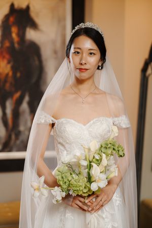 A bride in a white strapless wedding gown and veil holds a bouquet of green hydrangeas and white orchids.