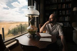 Person sits at desk by window with laptop and coffee, overlooking scenic desert landscape view.