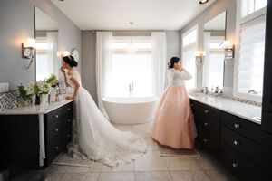 Two elegant dresses are showcased in a luxurious bathroom with a freestanding tub and dark wood cabinetry.