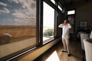 Person in white clothing looking through large window at desert landscape with dramatic cloudy sky.