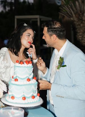 Newlyweds share a playful moment while cutting their white wedding cake decorated with red flowers.