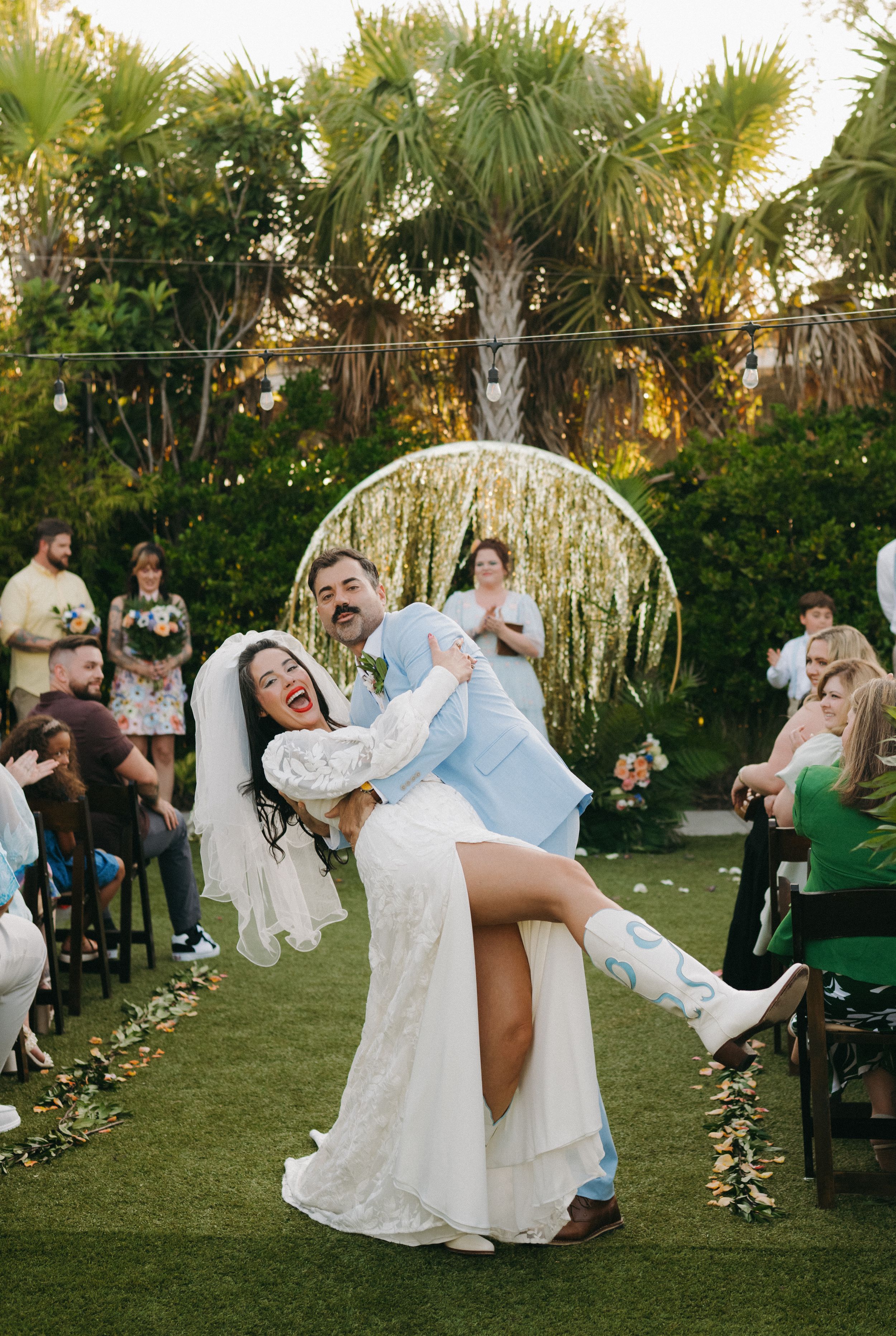 Wedding party performs dramatic dips during outdoor garden reception.