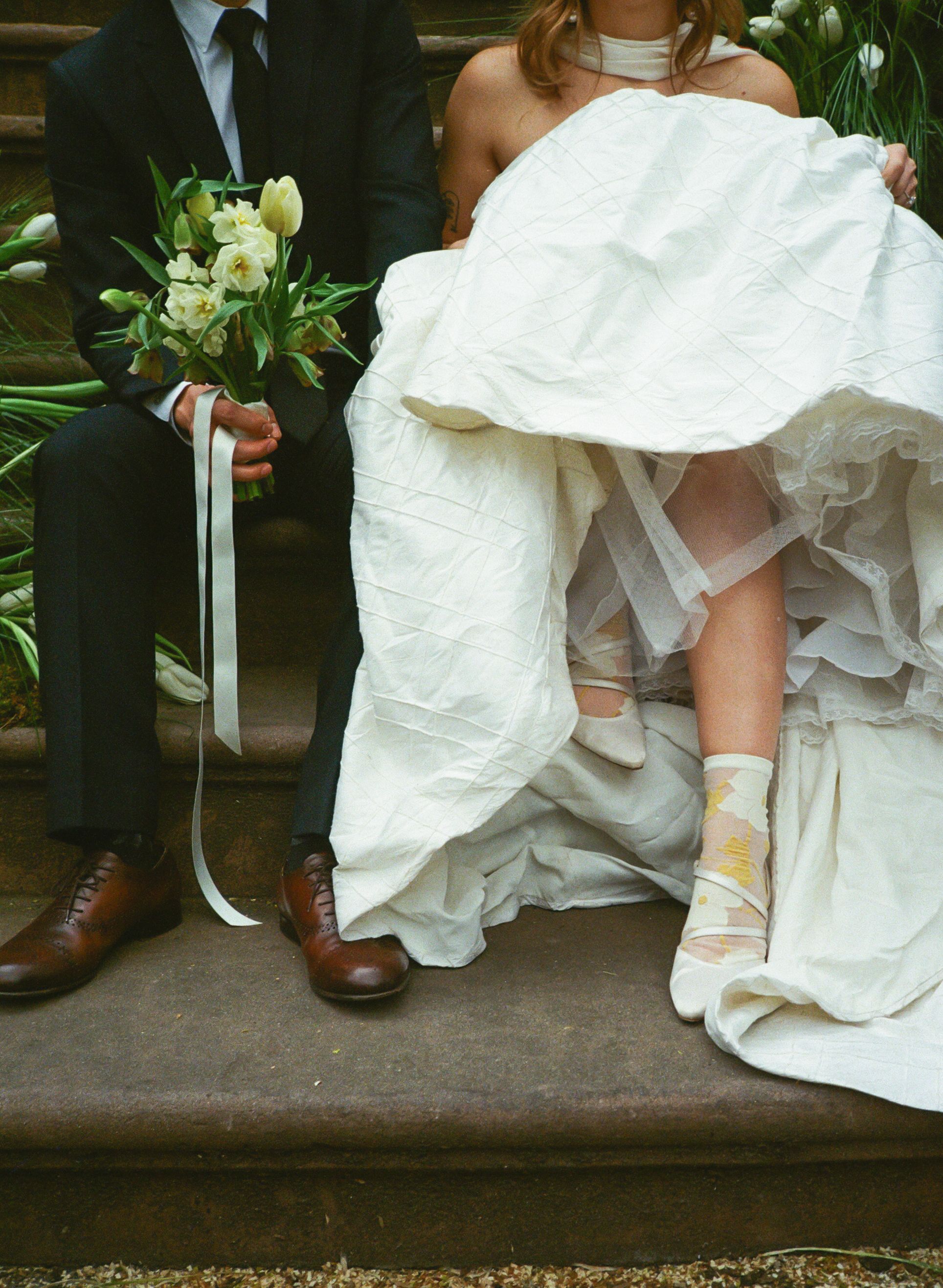 Detail shot of wedding dress hem and formal shoes on wooden steps.