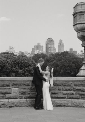 Black and white cityscape wedding portrait on stone wall overlooking urban skyline.
