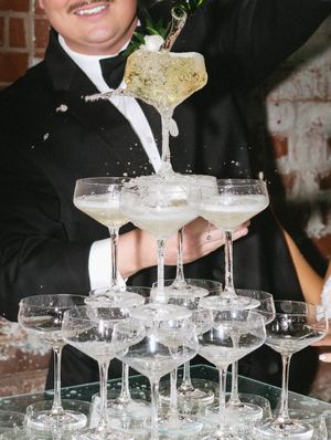 Champagne tower being filled with bubbly at an elegant wedding reception.