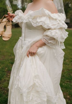 Close-up details of a layered white wedding dress with ruffles against green grass.
