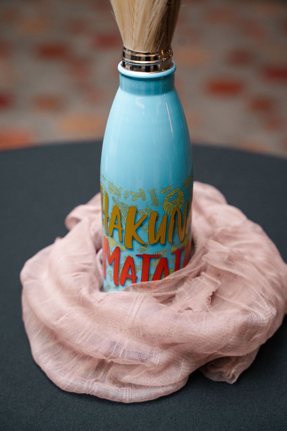 Sequence showing a blue glass bottle being wrapped in a soft pink fabric material against a dark background.