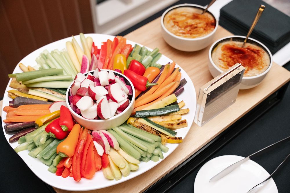 A colorful vegetable crudité platter with assorted fresh cut vegetables and dipping sauces served on a white plate.