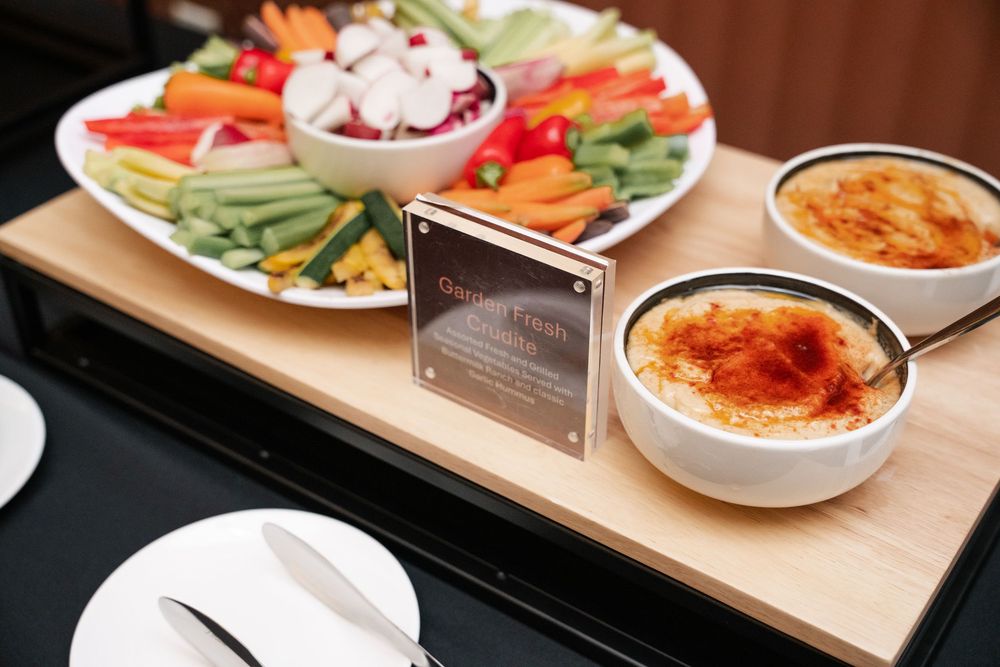 A wooden serving tray with fresh vegetable crudites and two bowls of creamy dipping sauce.