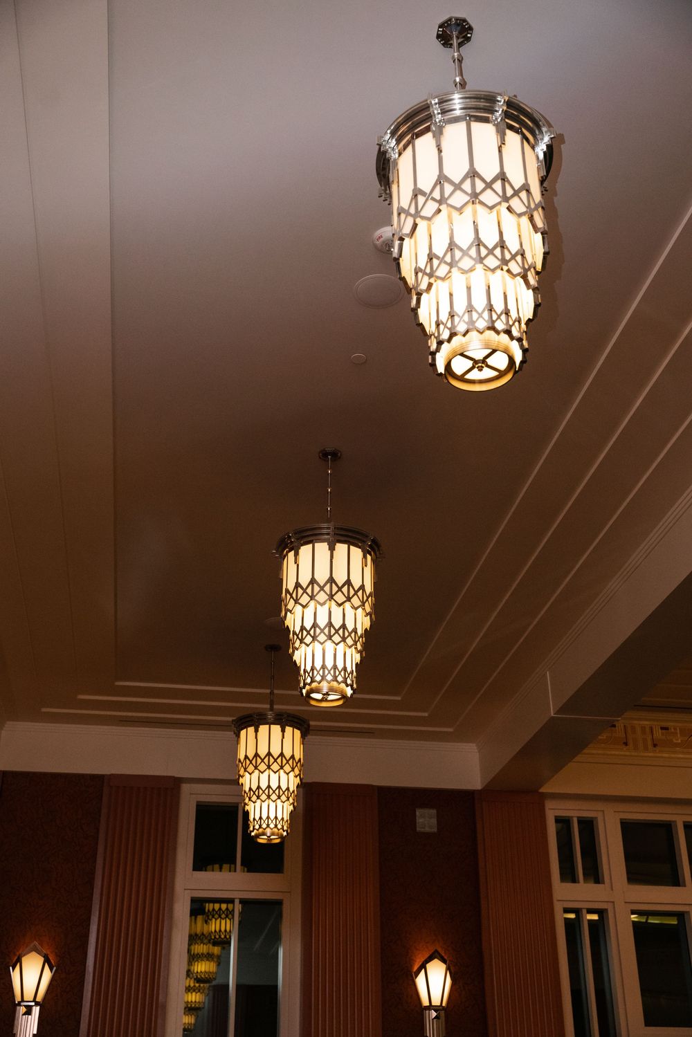 Art deco style crystal chandeliers hang in a row from a white ceiling creating elegant ambient lighting.