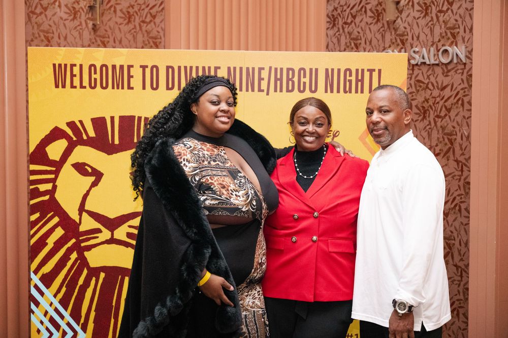 Three people pose in front of a Lion King Broadway show banner at a theater event.
