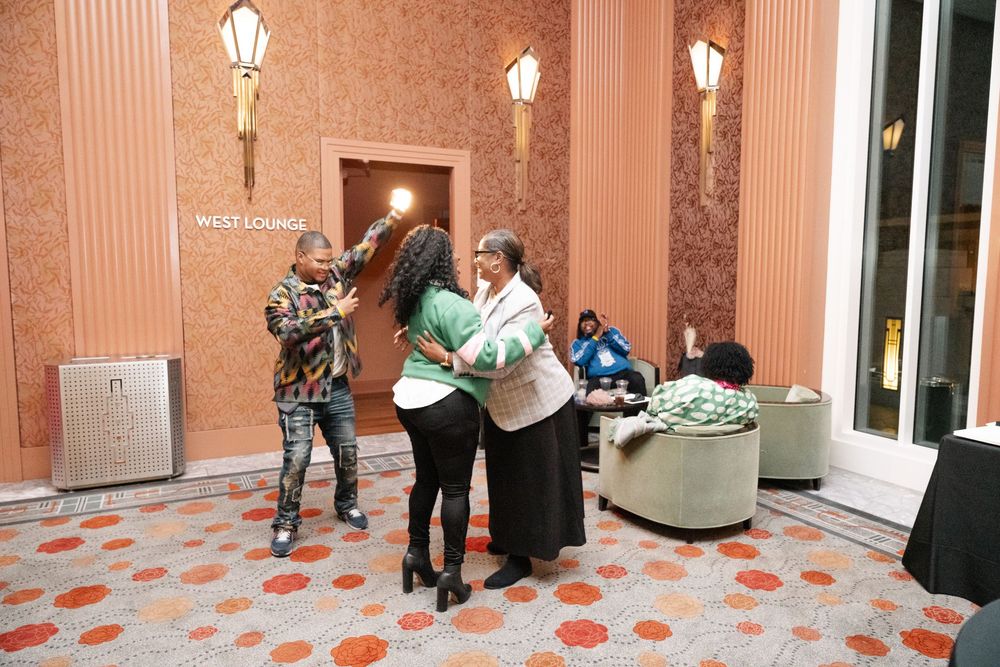 People interacting in an elegant hotel lobby with marble walls, decorative lamps, and a patterned floor.