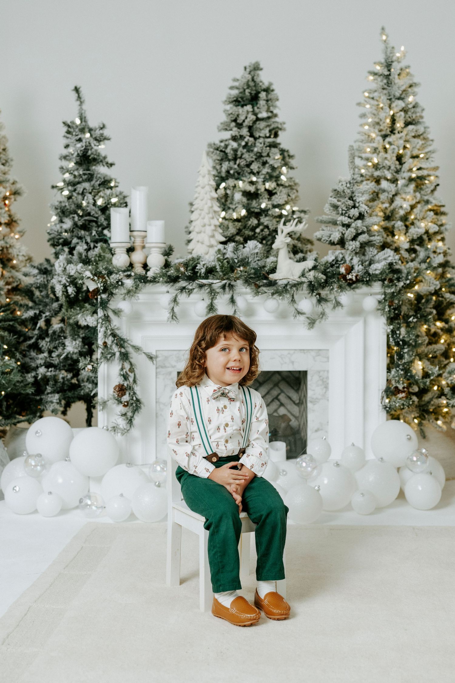 Festive holiday scene with decorated Christmas trees, white fireplace mantel, and white and green decor in a bright setting.