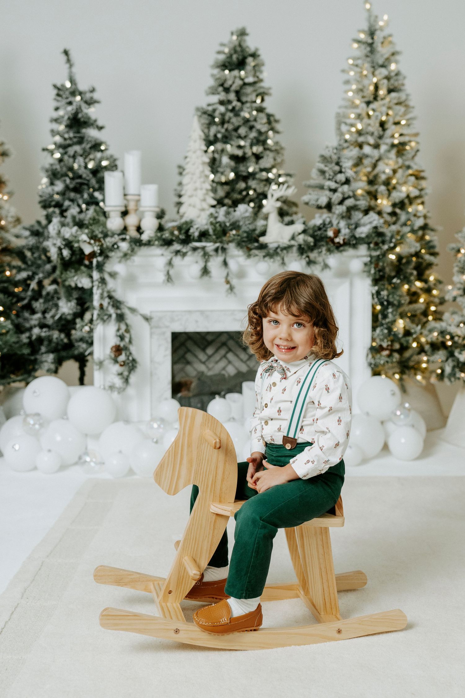 Festive holiday scene with rocking horse and decorated Christmas trees against white backdrop.