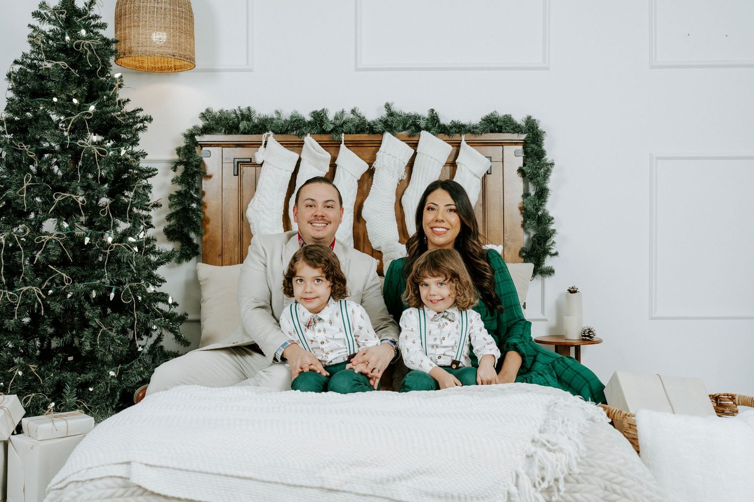 A group enjoying a cozy winter moment on a white bed with holiday greenery and decor in the background.