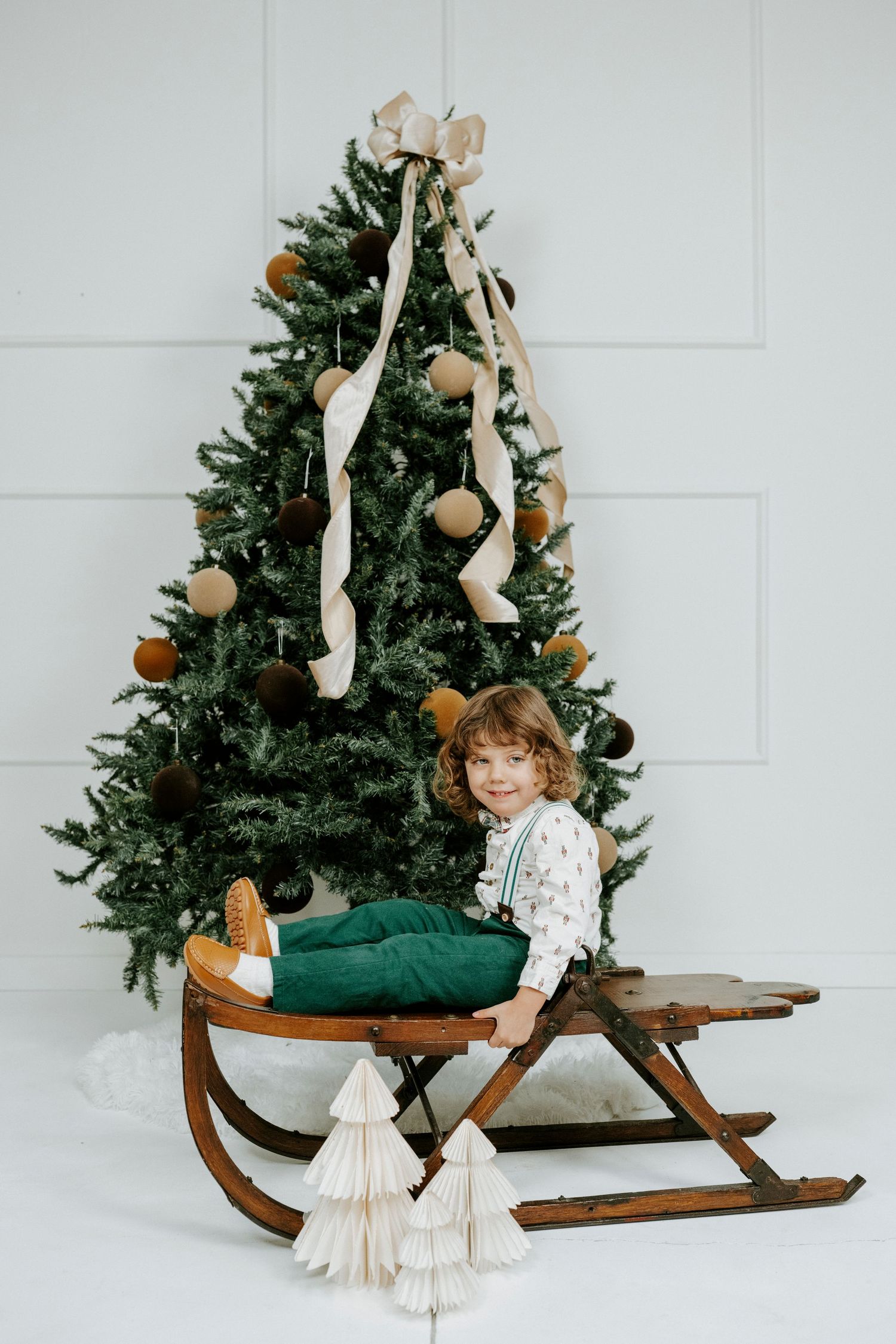 A rustic wooden sleigh decorated with a Christmas tree and ornaments in a minimalist white studio setting.