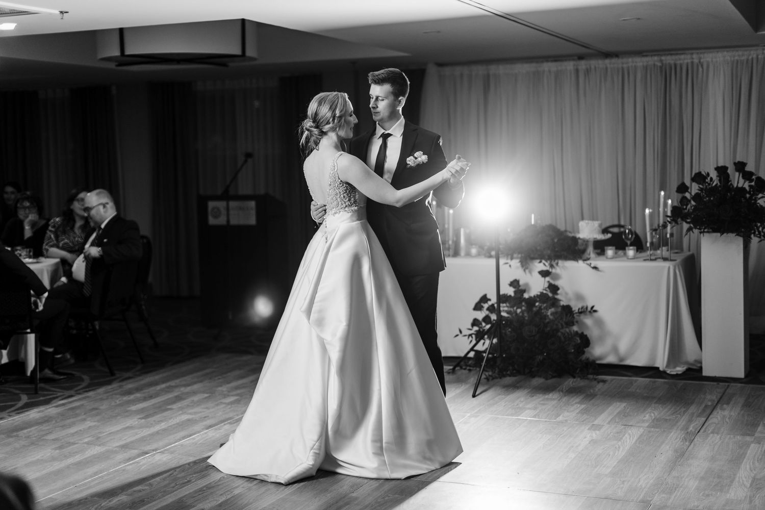 A couple shares their first dance at a wedding reception in a ballroom with dramatic lighting.