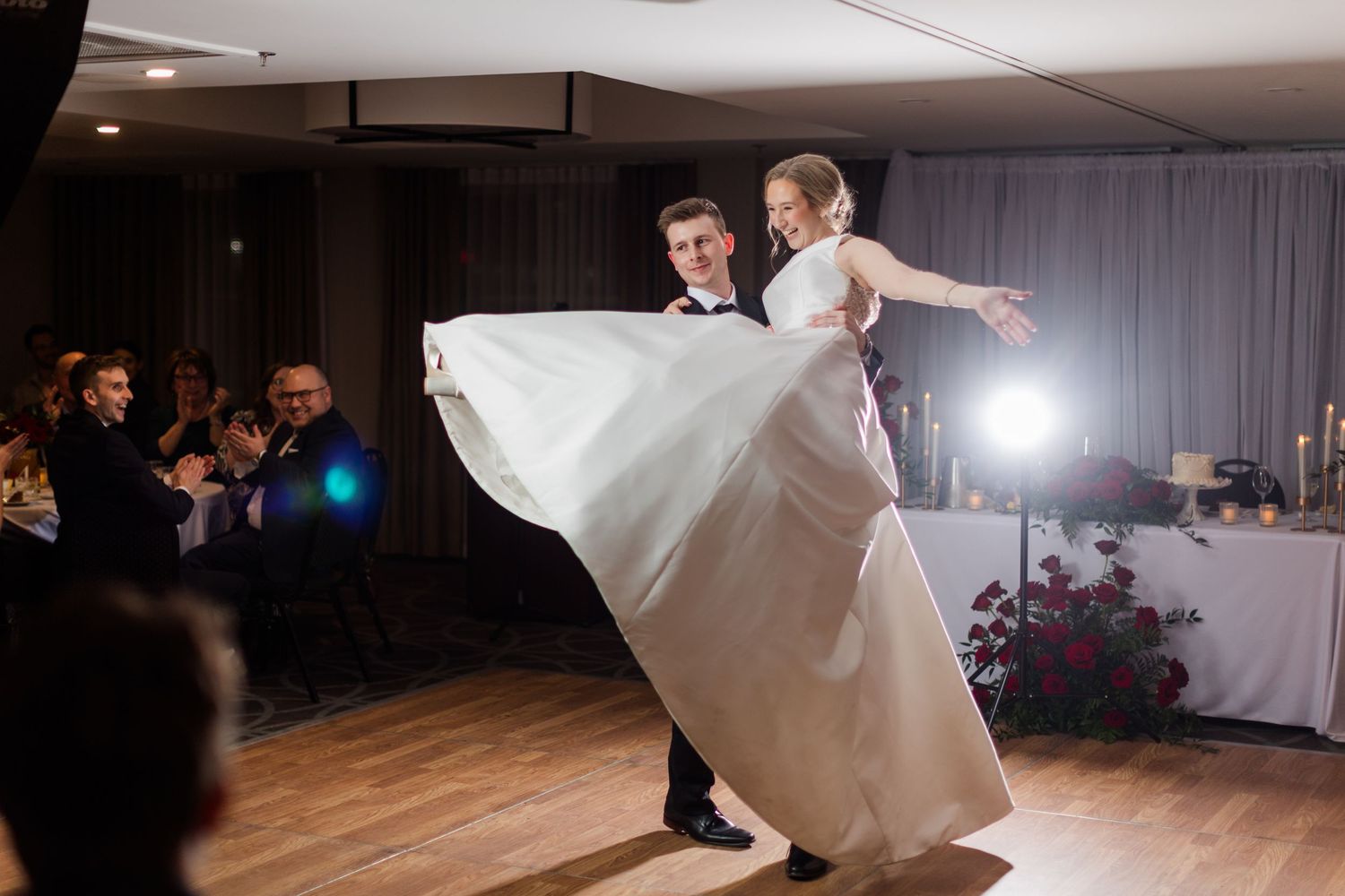A couple performs a dramatic dance lift during their first dance at an elegant wedding reception.