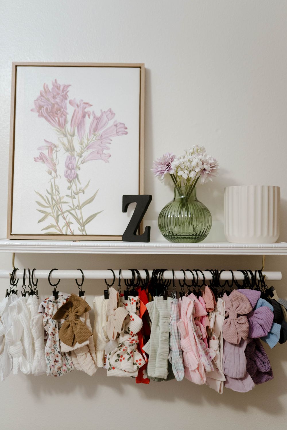 Nursery shelf with pink floral art, decorative letter Z, and baby clothes hanging below.