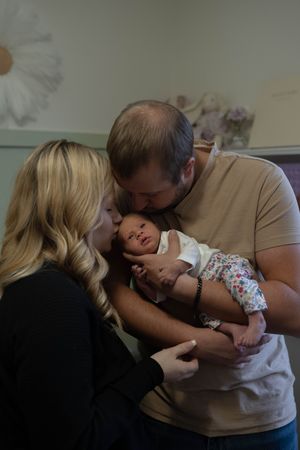 A tender moment captured as parents share affectionate kisses with their sleeping newborn baby.