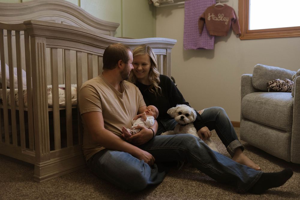 Family sitting on floor with white dog in nursery with wooden crib.