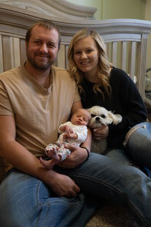 A heartwarming family portrait on a couch with their newborn baby and white dog.