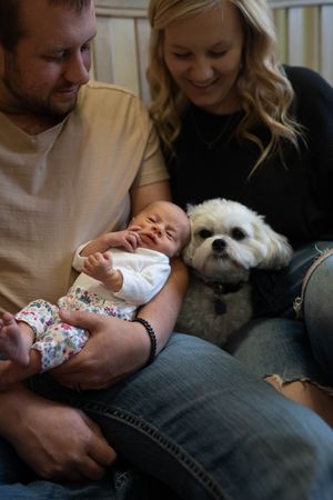 Candid family moments showing parents bonding with their newborn while their white dog watches.