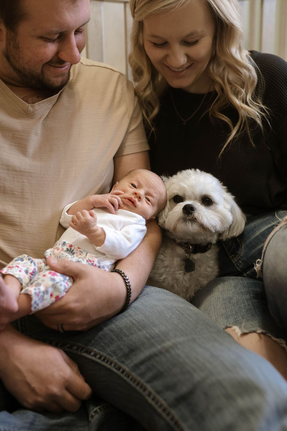 Candid family moment with sleeping newborn and white fluffy dog.