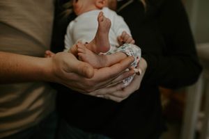 Gentle hands holding and cradling a sleeping newborn in soft lighting.